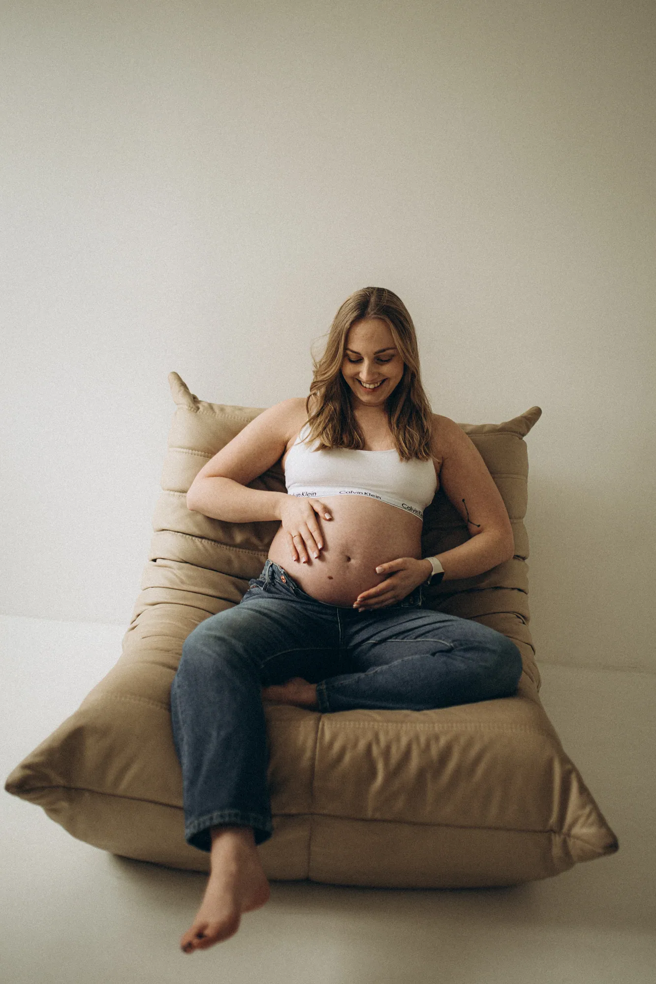 Sesja ciążowa Kraków - kobieta w ciąży siedzi na beżowej pufie